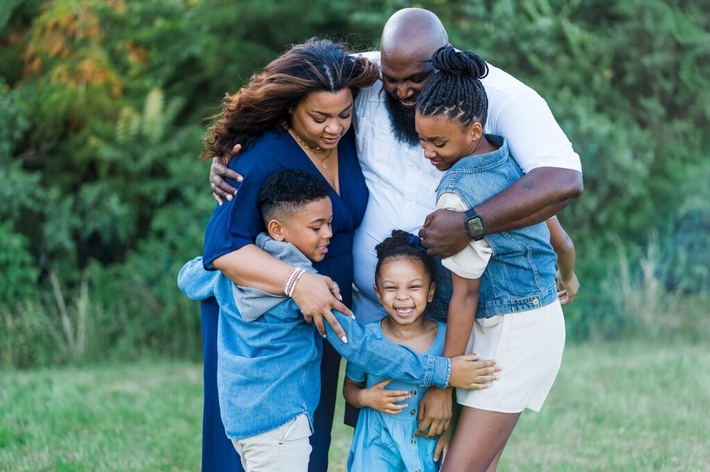 A loving family of five embracing in a field of green grass. The family is smiling and laughing, clearly enjoying each other's company. This image is a reminder of the importance of good relationships. 