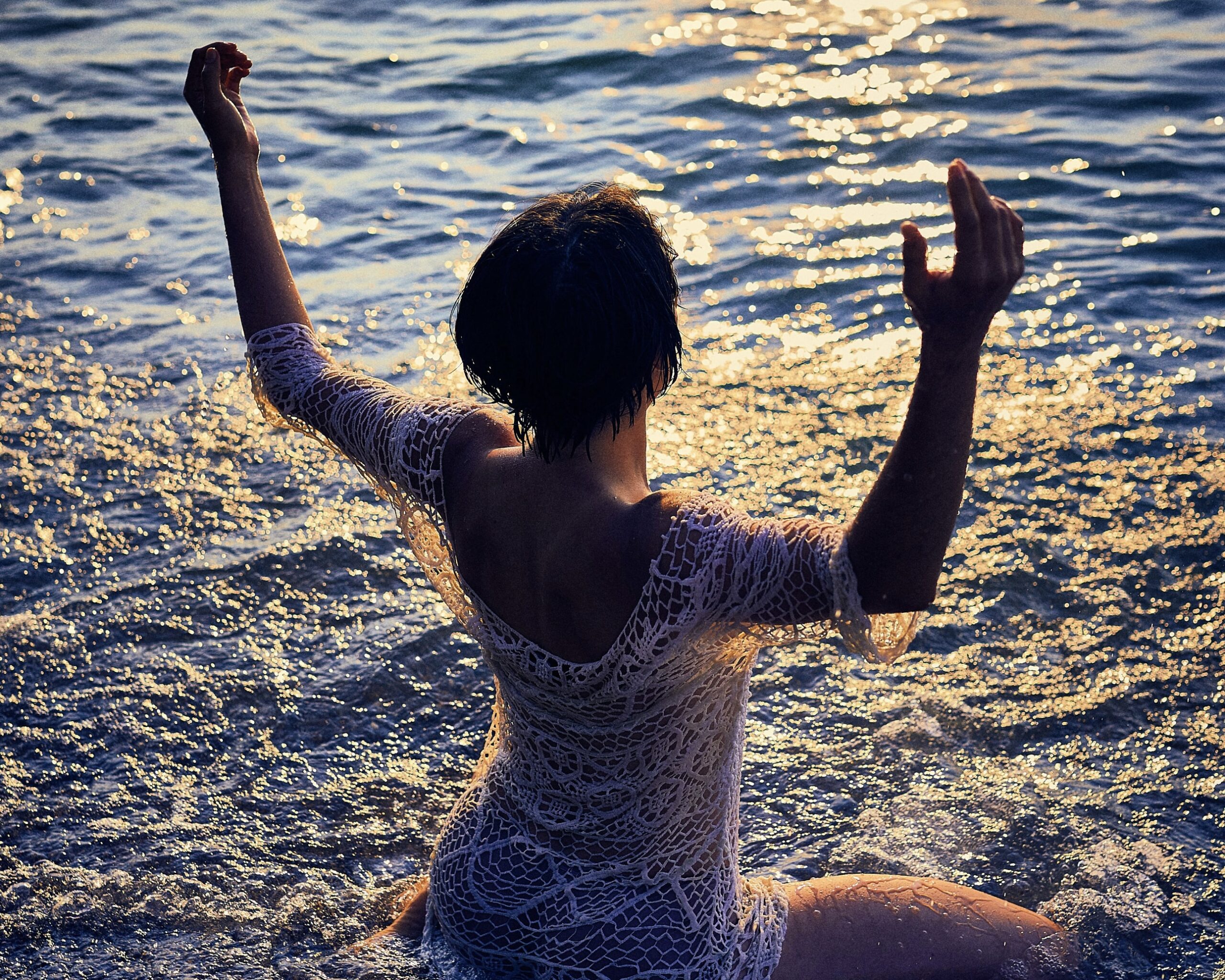 Woman with up-raised arms, kneeling at the edge of the ocean, surrendering and forgiving herself and others into the Light. 