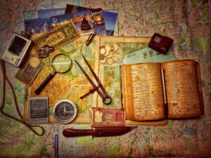 Vintage map image with everything you need to travel on a new adventure - novel, compass, magnifying glass, camera, and small knife.
