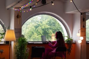 Woman of color very focused on typing on a laptop in front of an arched window.