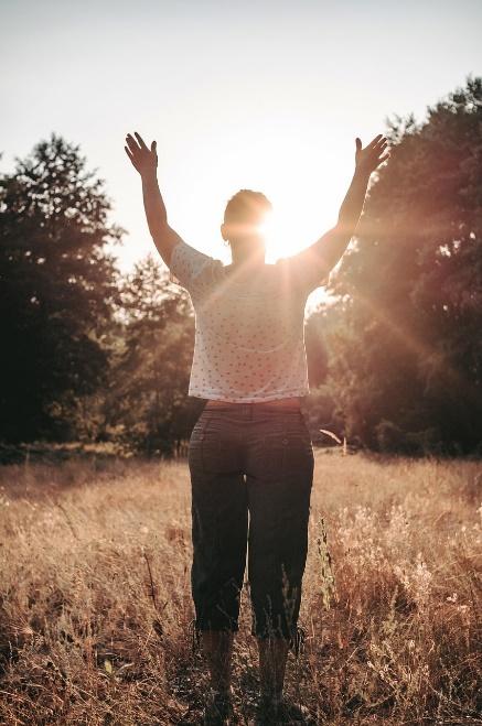 A person standing in a sunlit field with arms raised toward the Divine, bathed in warm sunlight, expressing joy, gratitude, or spiritual connection.