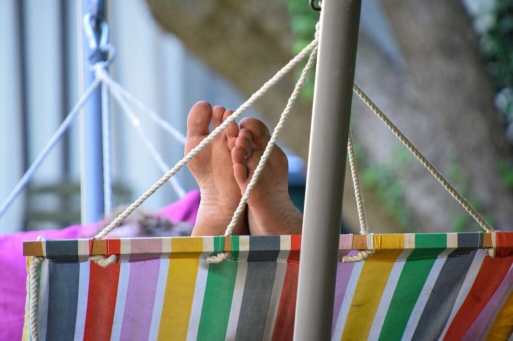 colorful striped hammock with someone's crossed feet peeking out over one end. Nothing else of the person is visible.